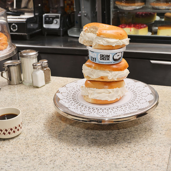 Oatly Cream Cheese in between stacked plain bagels with cream cheese.