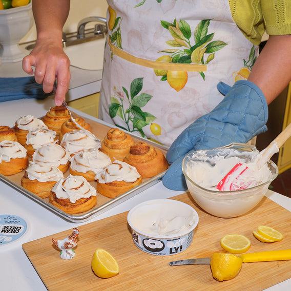 Person spreading oatly cream cheese on cinnamon rolls in the kitchen.